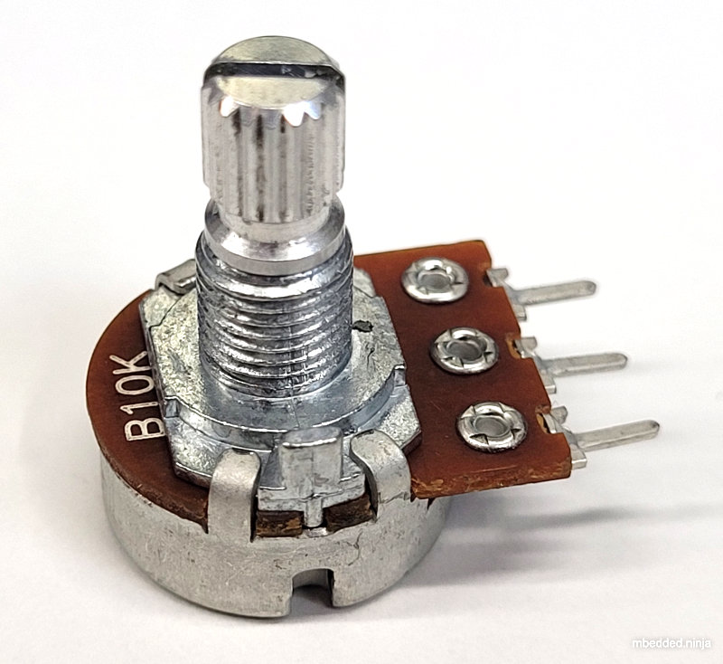 A photo of a panel-mount, through-hole potentiometer from BI Technologies/TT Electronics (part number P160KNP-0EC15B10K). The outer pins have a fixed resistance across them of \(10k\Omega\). The middle pin is connected to the wiper, and it's resistance varies between the outer pins (linearly in this case, but other tapers exist such as logarithmic) as the knob is turned.